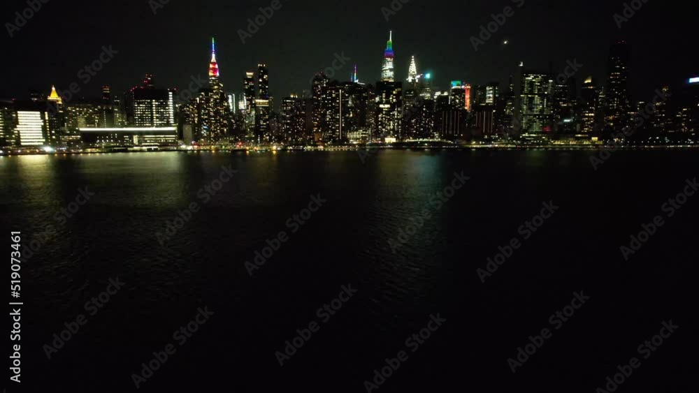 A high angle aerial view of Manhattan from over the East River in NY. It was taken on a quiet night with clear skies. The drone camera dolly in and pan left with buildings illuminated for pride month. A high angle aerial view of Manhattan from over the East River in NY. It was taken on a quiet night with clear skies. The drone camera dolly in and pan left with buildings illuminated for pride month.