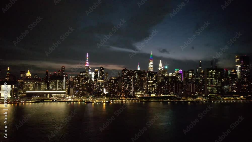 A high angle aerial view of Manhattan from over the East River in NY. It was taken on a dark night with reflective waters and cloudy skies. The camera dolly out and tilt down slowly. A high angle aerial view of Manhattan from over the East River in NY. It was taken on a dark night with reflective waters and cloudy skies. The camera dolly out and tilt down slowly.