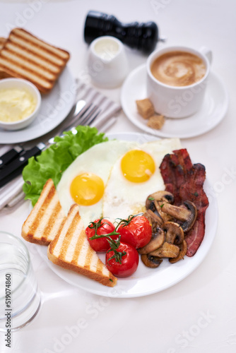 Fried eggs, bacon, tomato, toasted bread in white ceramic plate and cup of coffee