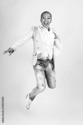 Beauty, style, business and fashion concept. Studio portrait of happy Thai woman with bright clothes, suit and torn jeans jumping in air. Model with shaved head. Black and white image with copy space
