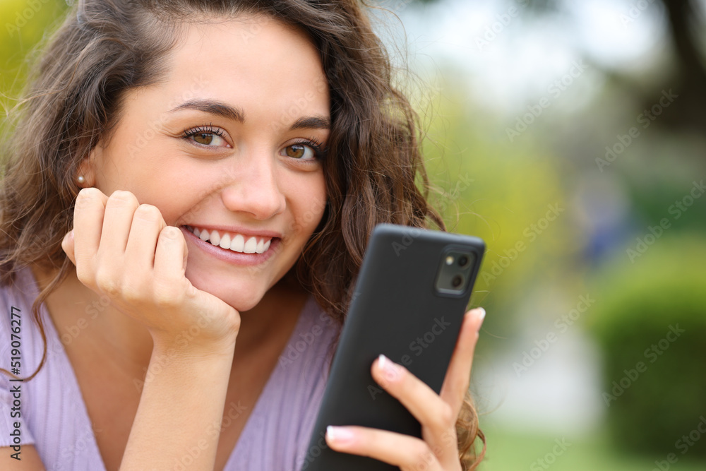 Happy woman holding cell phone looks at you Happy woman holding cell phone looks at you