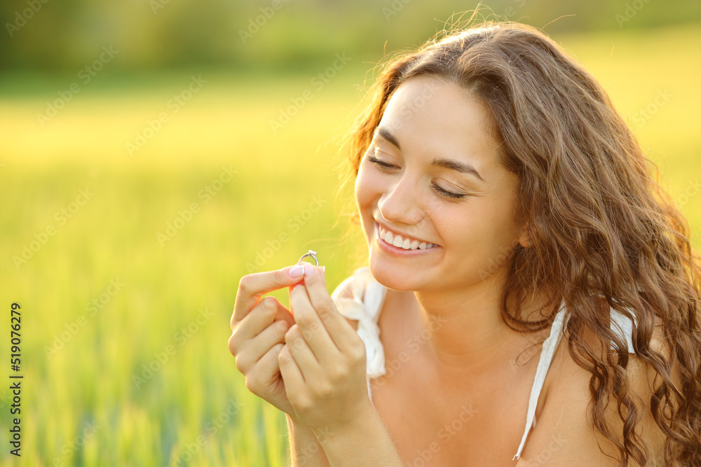 Happy woman looking at engagement ring in a field Happy woman looking at engagement ring in a field