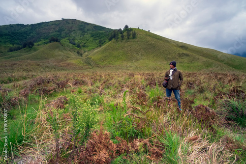 Photo of an asian man standing in the middle of meadow in mount bromo on a cloudy morning