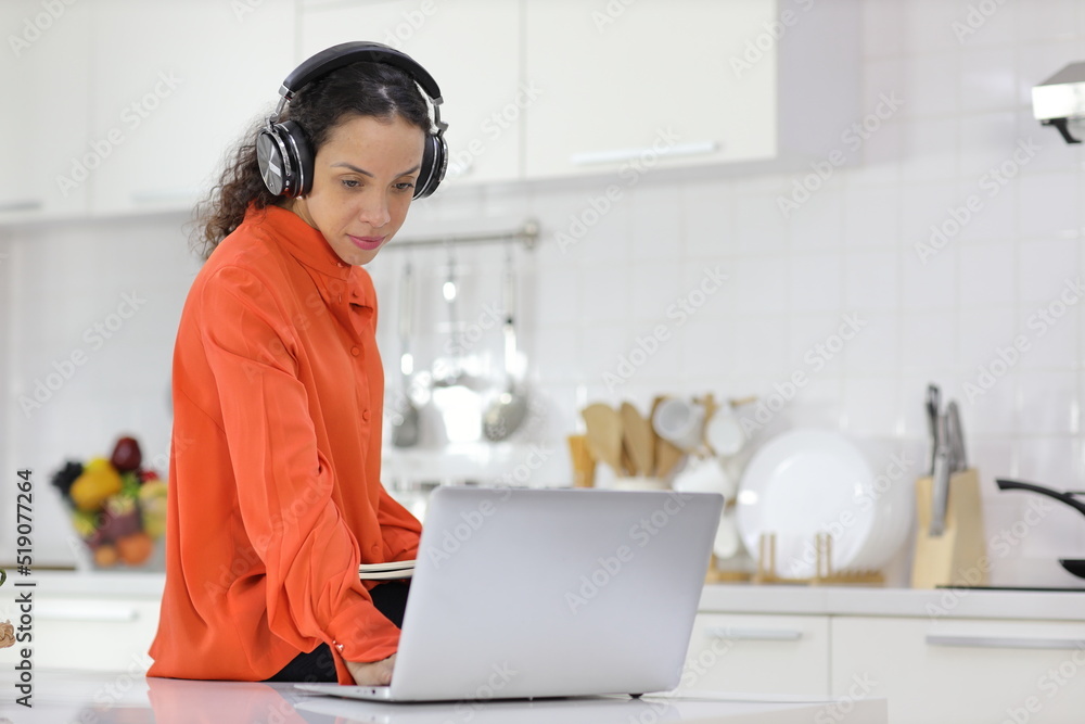 Happy latin woman learn cooking food while checking recipe from internet with computer in kitchen. Young female with headphone prepare delicious meal and listen music. Healthy and lifestyle concept Happy latin woman learn cooking food while checking recipe from internet with computer in kitchen. Young female with headphone prepare delicious meal and listen music. Healthy and lifestyle concept
