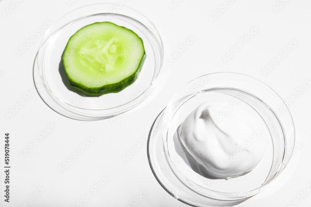 Cream, white color lotion and a piece of green fresh cucumber on a white background with bright light. Cosmetics for nourishing and moisturizing the skin. Cream, white color lotion and a piece of green fresh cucumber on a white background with bright light. Cosmetics for nourishing and moisturizing the skin.