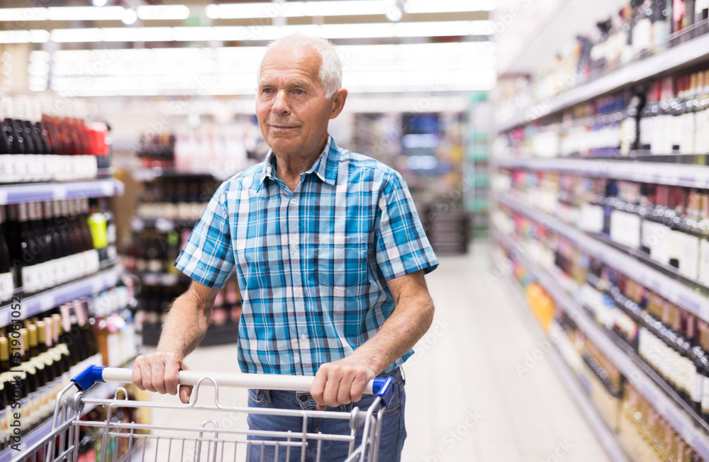 old age man examines bottle of vermouth in alcoholic section of supermarket