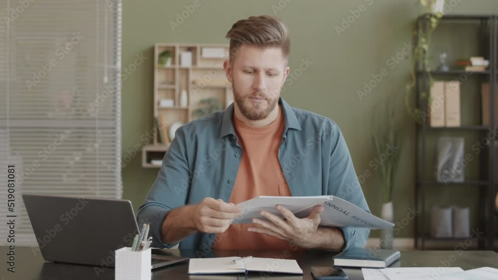 POV medium slowmo of Caucasian male marketing specialist talking at camera while examining annual report, sitting at office desk POV medium slowmo of Caucasian male marketing specialist talking at camera while examining annual report, sitting at office desk