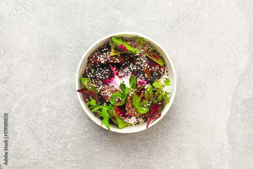 Salad of lettuce, beet and chicken liver with fresh radicchio and sesame seeds in a takeaway round container topped with yoghurt sauce on gray background. Healthy food delivery concept.