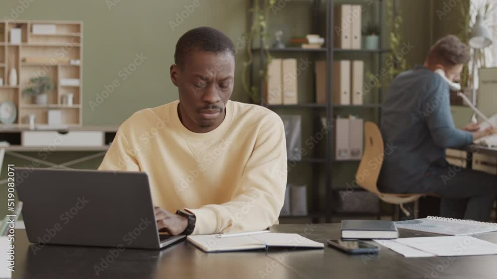 custom made wallpaper toronto digitalMedium slowmo of Black man in light yellow sweatshirt sitting at workplace typing on laptop and answering phone calls, working in digital marketing agency with colleague
