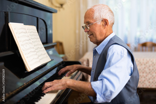 Elderly composer composes music and plays piano at home