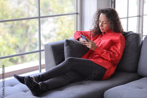 Smart and active latin woman sitting on sofa and using internet on computer with smart mobile phone in living room. Lifestyle with technology