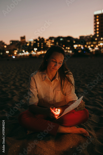 Woman burning paper with cigarette lighter sitting on beach at night photo