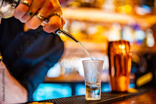 Fototapeta bartender pouring distilled alcohol into a shot glass in bar