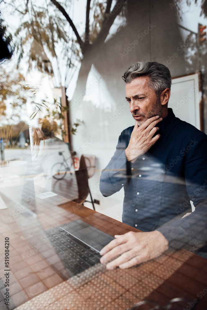 Thoughtful businessman looking at laptop in cafe Thoughtful businessman looking at laptop in cafe