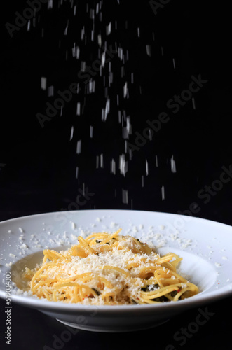 Studio shot of grated Parmesan pouring on plate of pasta