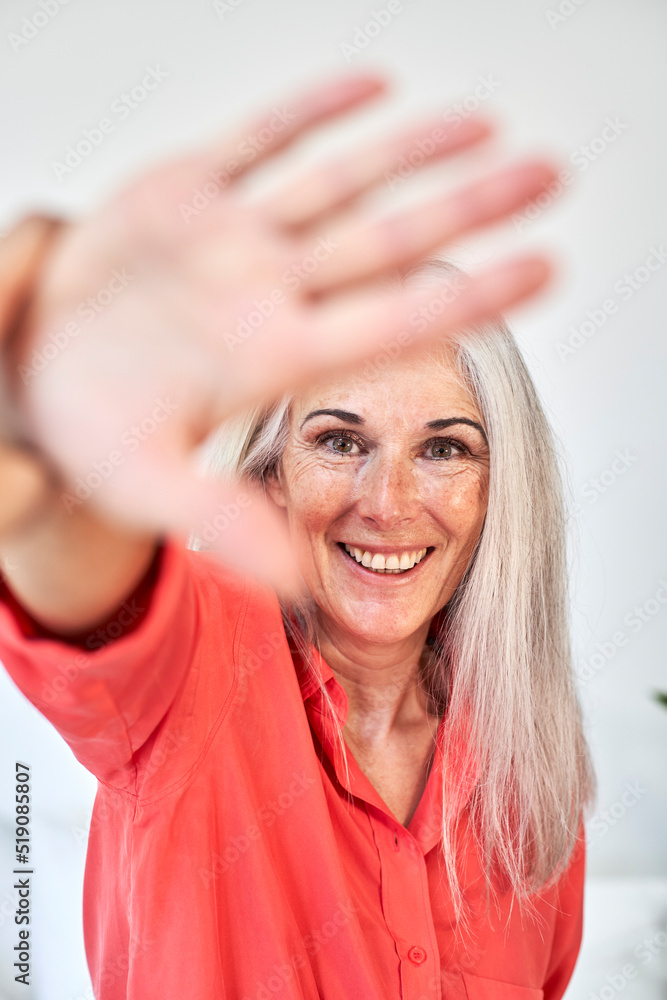 Happy mature woman showing stop gesture in front of wall Happy mature woman showing stop gesture in front of wall