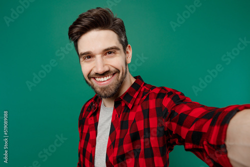 Close up young happy smiling caucasian man he 20s in red shirt grey t-shirt doing selfie shot pov on mobile cell phone isolated on plain dark green background studio portrait People lifestyle concept.