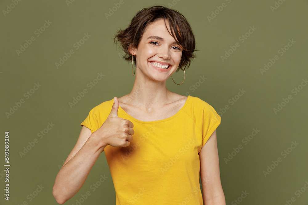 Young smiling satisfied cheerful fun cool happy woman she 20s wear yellow t-shirt showing thumb up like gesture isolated on plain olive green khaki background studio portrait People lifestyle concept Young smiling satisfied cheerful fun cool happy woman she 20s wear yellow t-shirt showing thumb up like gesture isolated on plain olive green khaki background studio portrait People lifestyle concept