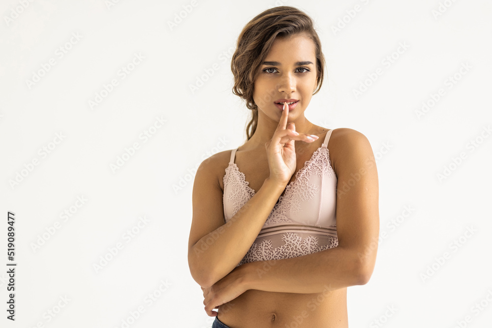 Fototapeta premium Curly woman smiling and showing silence gesture isolated over white background