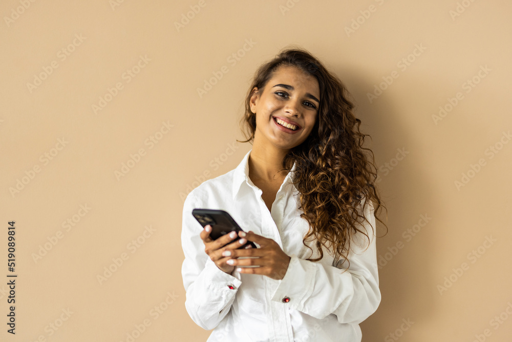 Romantic woman thinking with phone, looking aside and smiling dreamy, using dating app on phone, standing on beige background Romantic woman thinking with phone, looking aside and smiling dreamy, using dating app on phone, standing on beige background