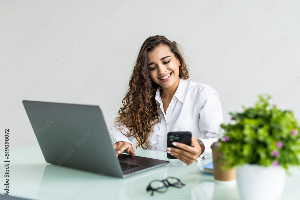 Young smiling business woman using smartphone near computer in office Young smiling business woman using smartphone near computer in office