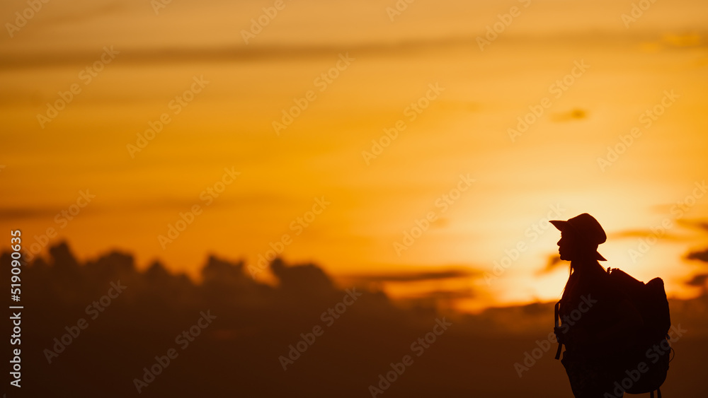 Young woman with backpack hikes in the mountain with a beautiful view through the sunset and warm red light. Blurred silhouette background.