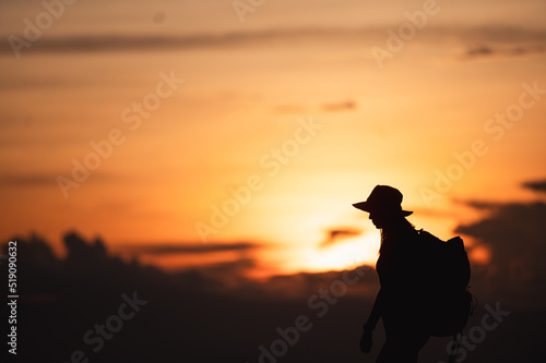 Young woman with backpack hikes in the mountain with a beautiful view through the sunset and warm red light. Blurred silhouette background.