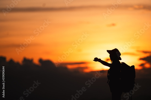 Young woman with backpack hikes in the mountain with a beautiful view through the sunset and warm red light. Blurred silhouette background.