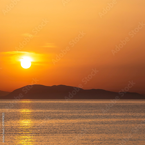 Sea beach and colorful sunset sky. Panoramic beach landscape. Tropical beach and seascape and a distant island in the background. Orange and golden sunset sky, calmness. © Dimitrios