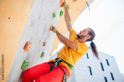 Young man climber on artificial climbing wall outdoors