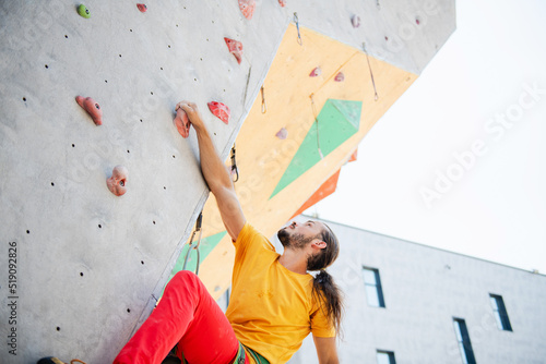Sportsman climber moving up on steep rock, climbing on artificial wall.