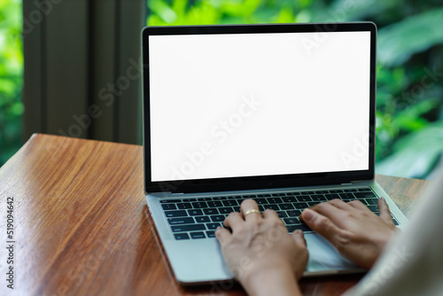 woman using and typing on laptop computer with blank white desktop screen on wooden table