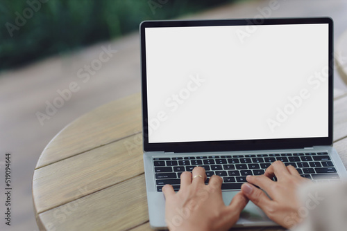 woman using and typing on laptop computer with blank white desktop screen on wooden table