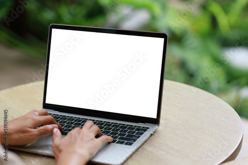 woman using and typing on laptop computer with blank white desktop screen on wooden table