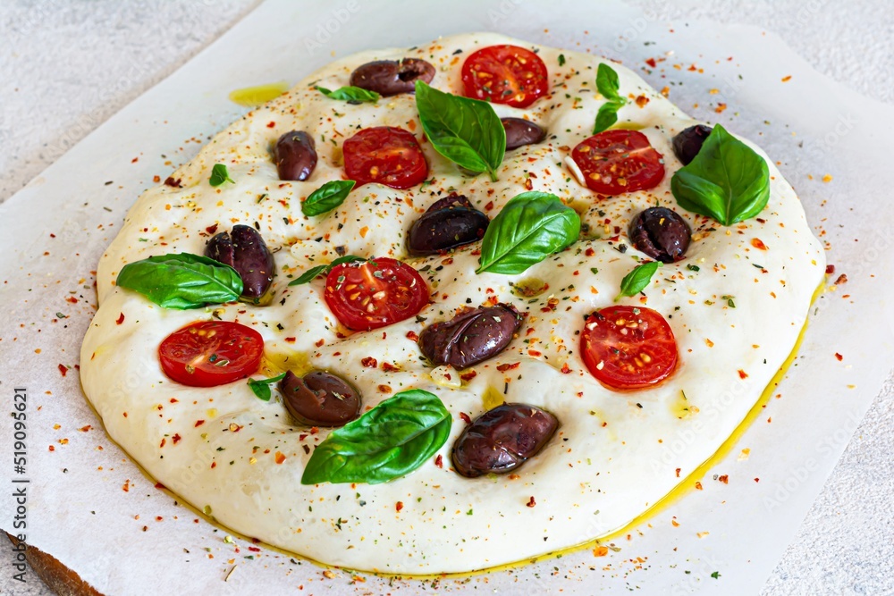 Fresh Italian flat bread (raw) Focaccia with tomatoes, olives, garlic and herbs on a wooden background. Fresh Italian flat bread (raw) Focaccia with tomatoes, olives, garlic and herbs on a wooden background.