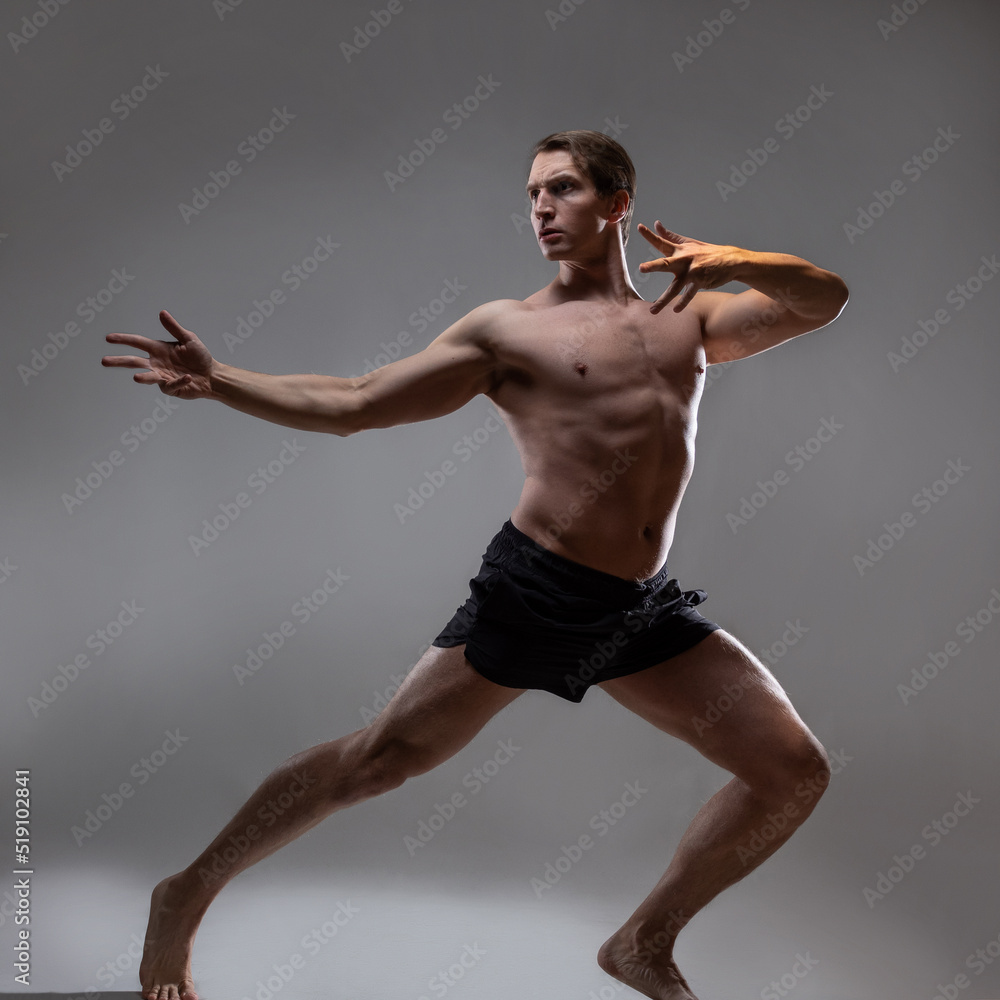 Obraz premium young muscular man in an expressive pose, artistic pose of the hero with outstretched arms. Beautiful muscles. extraordinary athletic body. Portrait on a gray background