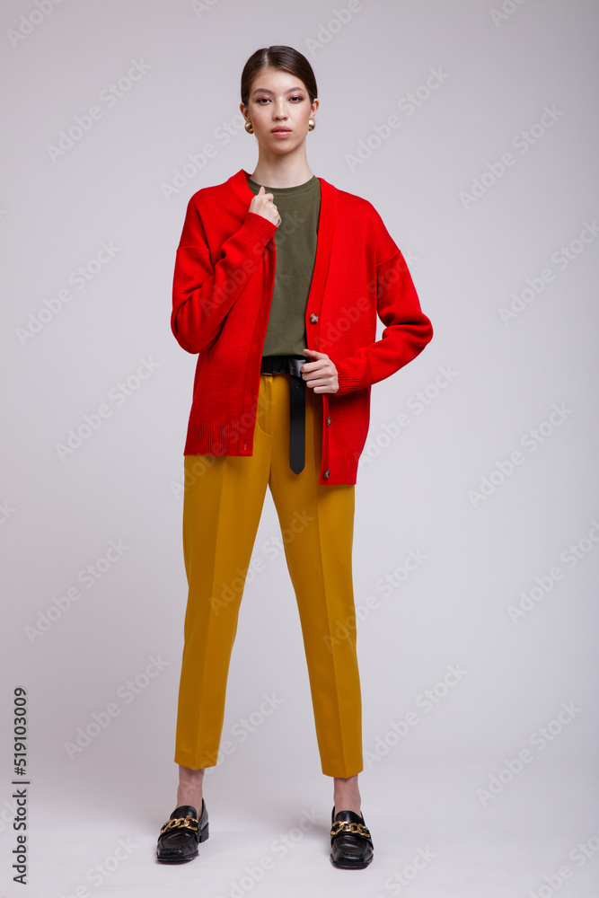 Fashion photo of a beautiful elegant young asian woman in a pretty yellow pants, red cardigan, green t-shirt, belt posing over white, soft gray background. Studio Shot. Fashion photo of a beautiful elegant young asian woman in a pretty yellow pants, red cardigan, green t-shirt, belt posing over white, soft gray background. Studio Shot.