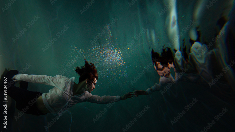 Photo underwater, a guy in a white shirt floundering underwater and reaching for the surface of the water, a man and his reflection. mystical underwater portrait - obrazy, fototapety, plakaty 