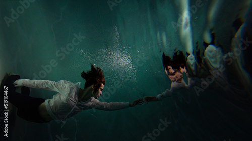 Photo underwater, a guy in a white shirt floundering underwater and reaching for the surface of the water, a man and his reflection. mystical underwater portrait