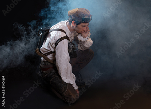 A guy in a steampunk image, a pilot or a mechanic. Retro style, fantastic image. portrait in smoke. Sitting on the floor