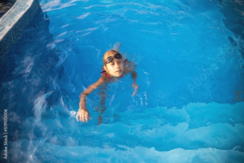 A girl in a bright swimsuit with swimming goggles dives into a pool with clear transparent water