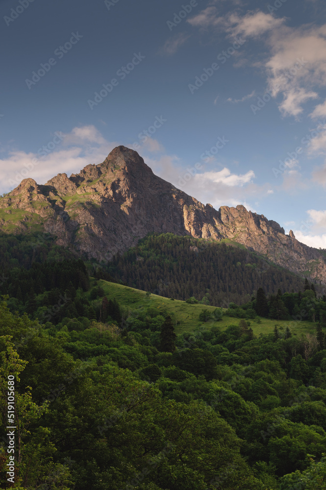 Fototapeta premium A beautiful sunset behind a mountain range at the base of which is a green dense forest