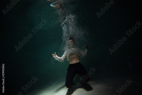 underwater shooting with contrasting light  a guy in a white shirt and pants screaming underwater  panicking and afraid of drowning  falling into the water  a crime.