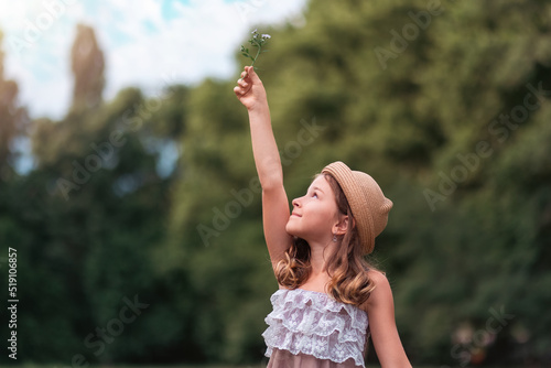 Portrait of a cute Caucasian small girl in a straw hat holding up a daisy flower. Copy space. The concept of peace, freedom, childhood, Earth Day and Summer