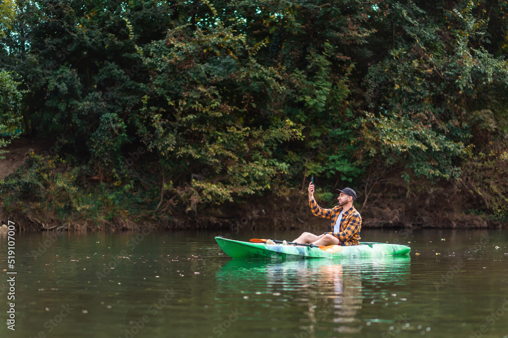 A frustrated caucasian bearded man is sitting in a kayak and holding a phone in his hands, trying to catch a mobile connection. Copy space. Concept of problem in trip