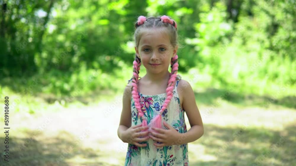 A little girl stands in the fresh air and strokes her rose braids. Weaving pigtails with artificial hair A little girl stands in the fresh air and strokes her rose braids. Weaving pigtails with artificial hair