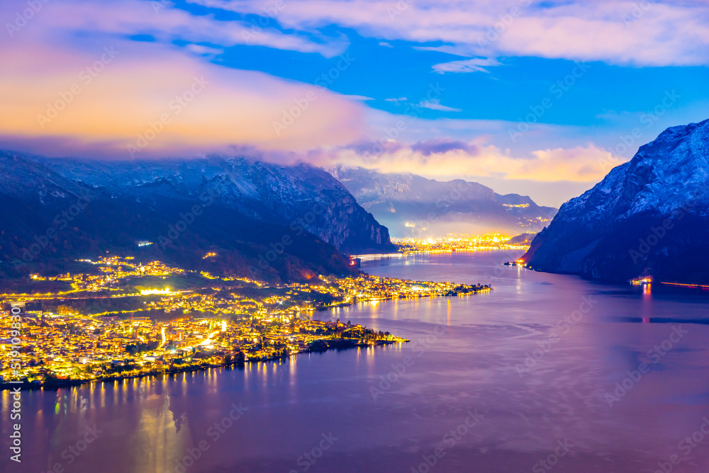 Panorama showing the Lecco shore of Lake Como, on a winter evening, with clouds and snow capped mountains.