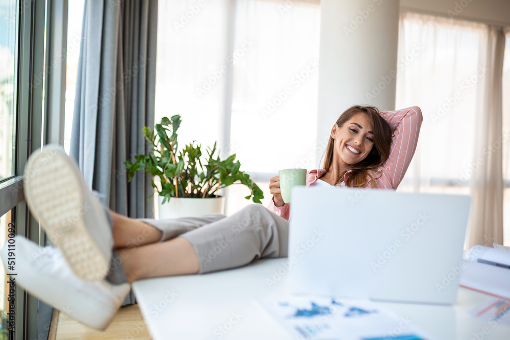 Young pretty businesswoman in the office sitting in office chair, hands up and with her feet up on a desk enjoying coffee Young pretty businesswoman in the office sitting in office chair, hands up and with her feet up on a desk enjoying coffee