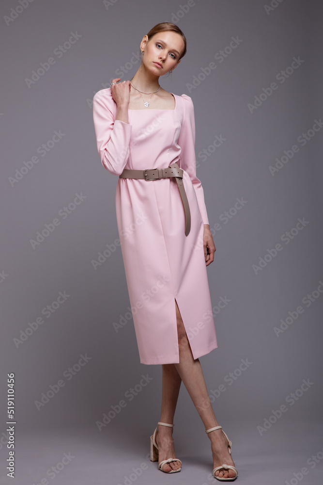 Fashion photo of a beautiful elegant young woman in a pretty pink dress, belt, shoes posing gray background. Studio Shot. Portrait Fashion photo of a beautiful elegant young woman in a pretty pink dress, belt, shoes posing gray background. Studio Shot. Portrait