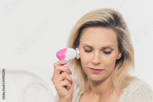 Closeup portrait of a European woman doing her skin care routine. Beautiful blonde caucasian middle-aged girl using a face massager. High quality photo